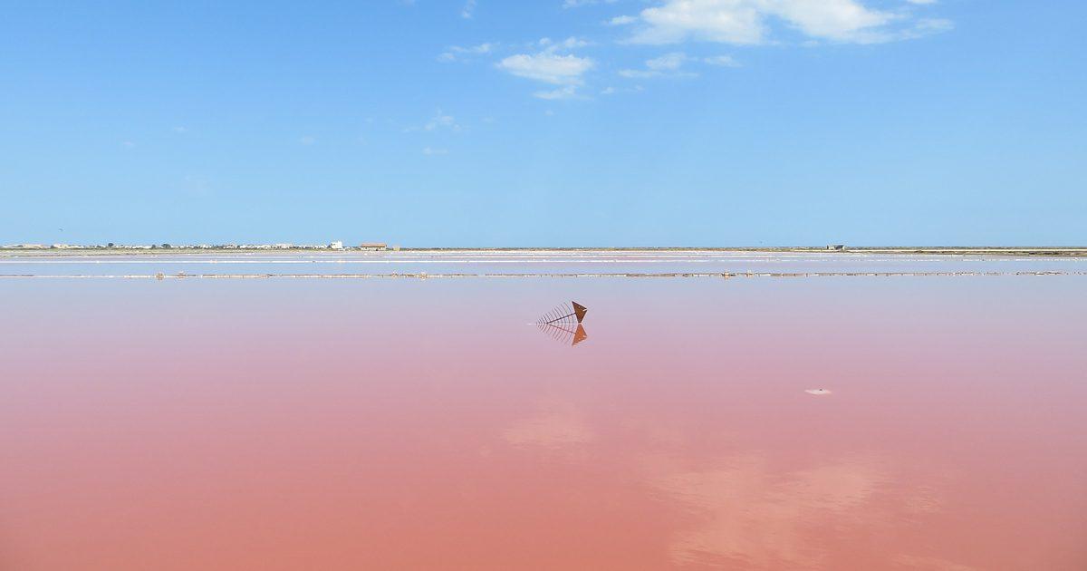 Gruissan salt pans: a pink basin reflecting a rusty structure, with a village in the distance under a big blue sky